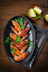  Baked chicken wings with sesame seeds, parsley and lime on a black plate top view, vertical photo