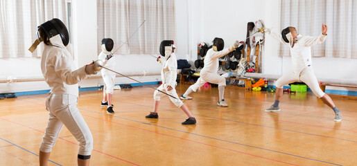 Portrait of young fencers with instructor engaged in fencing in training room