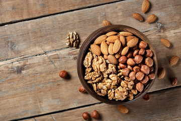 Various nuts in wooden bowl on wooden background, top view, copy space