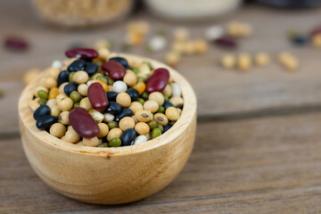 Various grains such as soybeans, black beans, red beans, dried corn in a wooden cup on a wooden table background.
