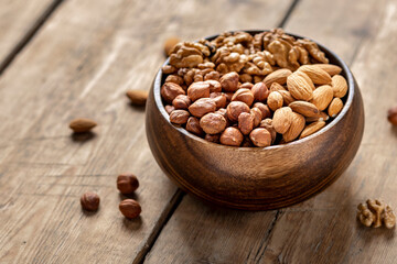 Nuts assortment - hazelnuts, walnuts and almonds in wooden bowl on wooden background, copy space