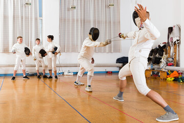 Fototapeta premium Two fencing instructors showing to young fencers effective techniques in a training room