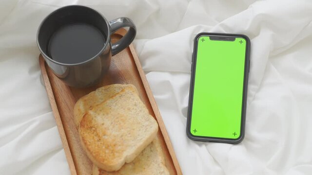 smartphone with chromakey screen for advertising. coffee and bread for breakfast in the bedroom.