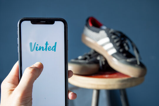 Iphone with vinted logo on screen with hand in front of style shoes. Vinted is a Lithuanian online marketplace and community for second hand clothes, accessories