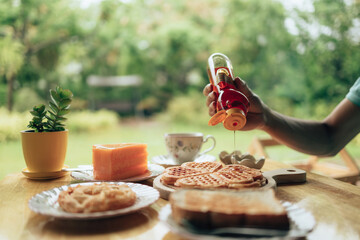 Hand pouring honey on fresh waffles on wood plate. Waffle and dessert concept.