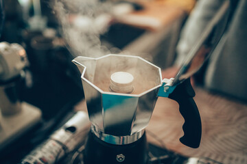 Brewing black moka coffee using moka coffee maker and boiling with smoke on gas stove.