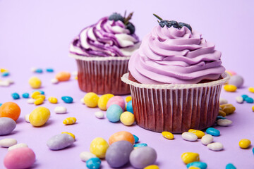 Blueberry cupcakes and colorful candies on lilac background
