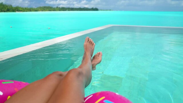 Travel vacation concept with bikini woman relaxing swimming in luxury infinity pool of Tahiti resort hotel lying in water floating on donut float in red bikini. Tanned slim body and hot legs