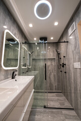 Modern luxury bathroom with black double shower, massage jets, rain shower head,  double sink, and shower door. 