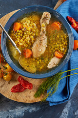 Pea soup with chicken, carrots, tomatoes and herbs in a deep plate on wooden board with napkin on blue background