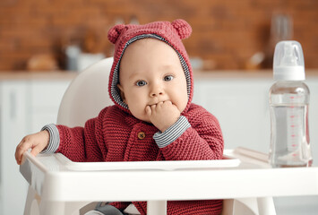 Cute little baby with bottle of water in kitchen