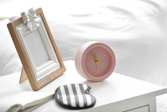 Alarm clock with photo frame and sleeping mask on table in bedroom