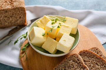 Bowl with fresh butter and bread on wooden board, closeup