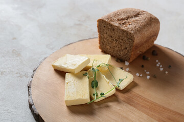 Wooden board with fresh butter and bread on light background