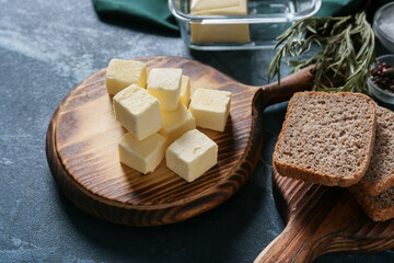 Fototapeta premium Cubes of fresh butter on wooden board with sliced whole wheat bread, rosemary and sea salt on dark rustic table