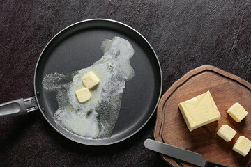 Frying pan and wooden board with fresh butter on dark background