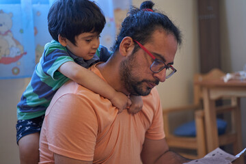 Father reads furniture assembly instructions while his son hangs by his neck. Assembling furniture at home. Parenting