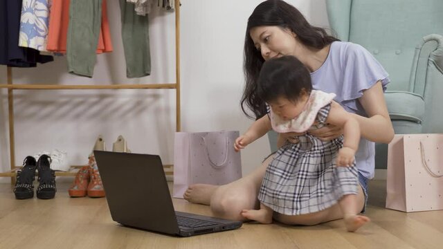 cute curious child who is carried away from the laptop is crawling back to bother her mother as she is shopping online on the floor. 
