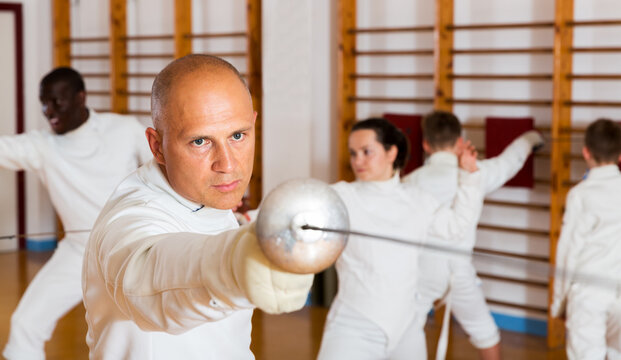 Male athlete training attack movements with rapier at fencing workout in gym