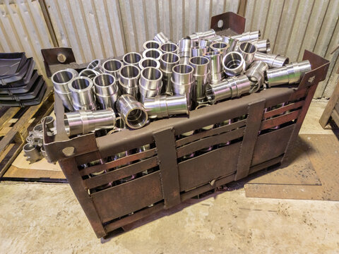 shiny steel parts overflowing big intermodal steel container box on factory floor