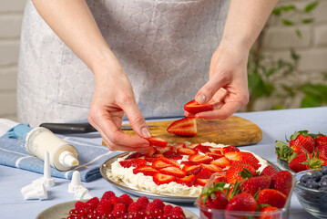 woman baker stacks strawberries on meringue strawberry cake base. Homemade strawberries cake made from meringue cake and cream with strawberries. home cooking concept