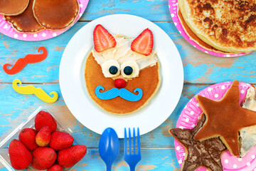 Fun food for kids. Cat shaped pancakes with berries and peanut paste on blue wooden table, top view. Healthy vegetarian food for children.