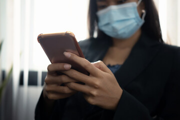 Cropped shot of businesswoman in protective mask using mobile phone in office.
