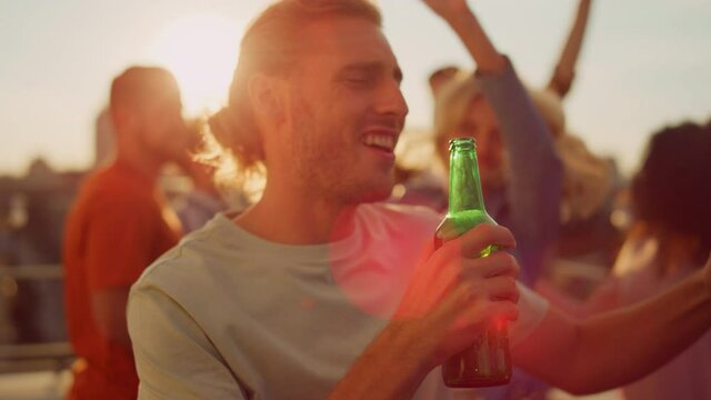 Cheerful man drinking beer at rooftop party. Happy guy dancing outdoors. 