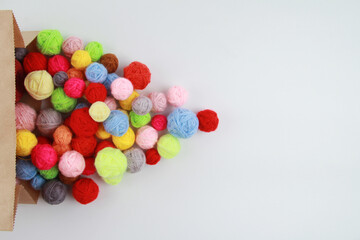 Lots of colorful, scattered wool balls of knitting yarn from a paper bag on a white background. The concept of handwork, needlework and crafts. Top view. Flatley. Copyspace.