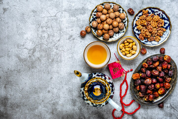 Obraz na płótnie Canvas Popular food during Iftar - macadamia nuts, pistachios, walnuts, dry dates. Karan, rosary, teapot, bowl with black tea on concrete background Top view Flat lay Muslim holiday of holy month of Ramadan