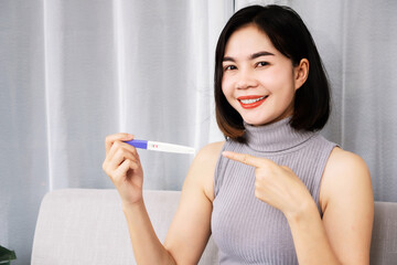 happy Asian woman smiling hand holding at pregnancy test showing positive result