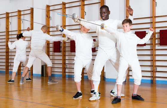 Focused diligent positive boys fencers attentively listening to professional efficient friendly fencing coach in gym