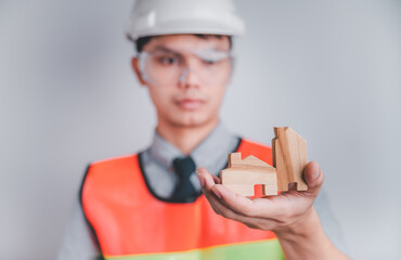 Engineer wears a reflective vest. Glasses and helmets. In his hand held a model of a wooden house...