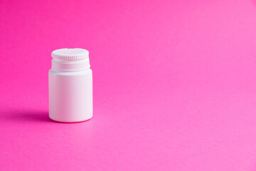 White jar of pills or vitamins on a pink paper background. Medicine on background with copy space.