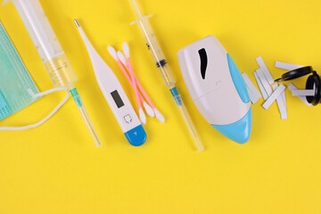  Medical disposable mask, thermometer, cotton buds, glucose meter test strips, syringes, nebulizer in yellow background close up.
