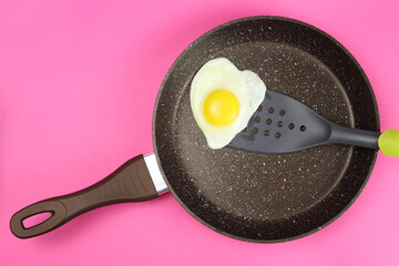 Fried egg in a frying pan on a pink background