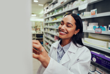 Cheerful female pharmacist wearing labcoat searching for medicine in shelf in chemist