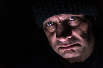 A brutal portrait of a man on a black background in a knitted hat, blurred. Strong-willed male gaze. The eyes of a man.