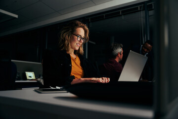 Portrait of a happy young female business executive using laptop in modern office