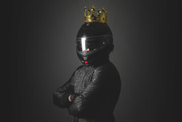 Motorbiker in a helmet with a golden crown on his head on a dark background. Arrogant driver concept. Race winner.