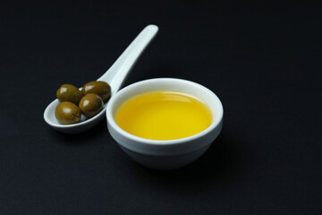 Spoon with olives and bowl of oil on black background
