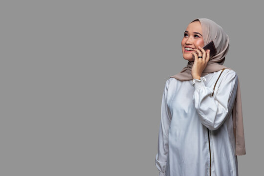 Beautiful Woman Wearing Hijab Is Making A Phone Call With A Smiling Expression While Looking Up Isolated On Plain Background