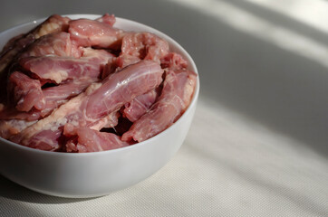 Raw chicken necks in a white ceramic bowl on a light background.