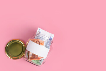 Euro banknotes in glass money jar with blank label, financial, saving. Money box with empty sticky note paper. Jar full of cash, save money concept, expense planning and control, free space for text