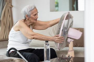 Overheated asian senior woman sweating,high temperature in sunny day while stay at home,cooling herself in front of an electric fan,old elderly suffering from heat,hot summer weather,lifestyle concept - obrazy, fototapety, plakaty