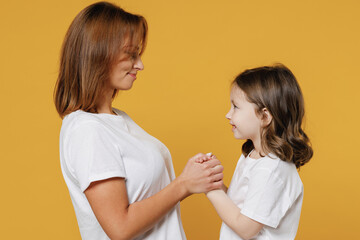 Happy woman in basic white t-shirt have fun with cute child baby girl 5-6 years old hold hands. Mommy little kid daughter isolated on yellow color background studio. Mother's Day love family concept.