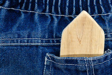 Homemade wooden house toy in the pocket of blue jeans. The concept of eco-friendly toys, the concept of buying a house, a house in your pocket.