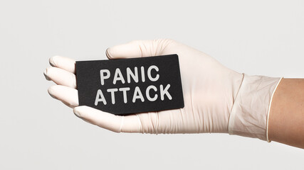 Closeup of the hand in a white sterile glove holding a card with text - PANIC ATTACK
