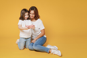 Obraz na płótnie Canvas Full body length happy woman in white t-shirt have fun sit use cell phone child baby girl 5-6 years old Mom mum little kid daughter isolated on yellow color background studio Mother's Day love family