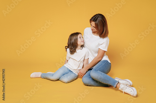 Full body length happy woman in basic white t-shirt have fun sit on floor with child baby girl 5-6 year old Mom little kid daughter isolated on yellow color background studio Mother's Day love family
